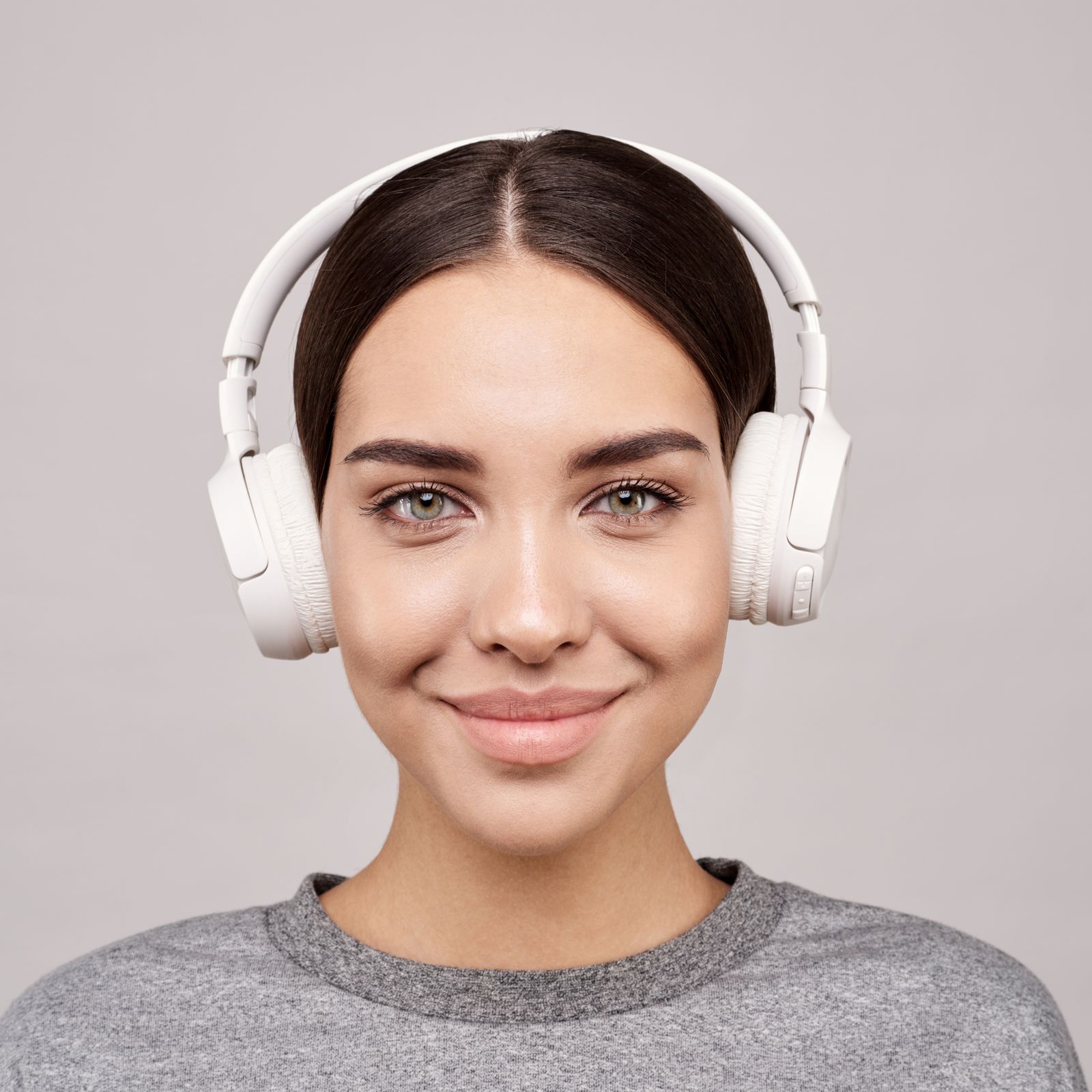 Person wearing white over-ear headphones against a plain studio background