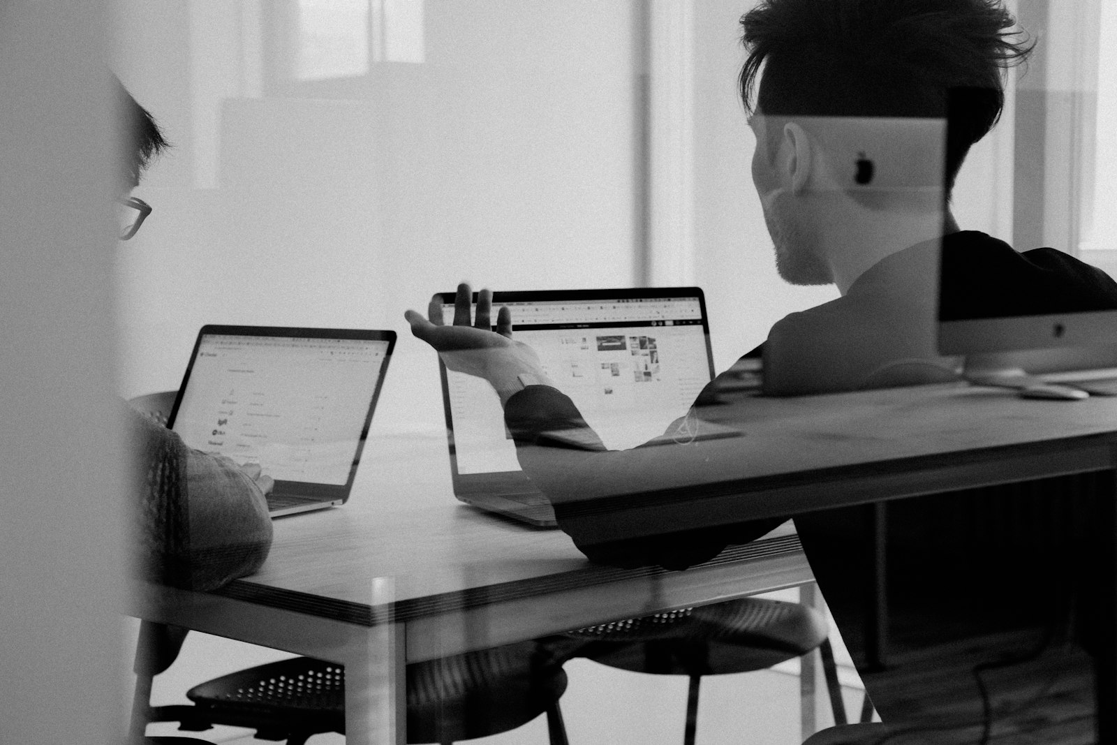 Two colleagues collaborating on laptops in a modern office