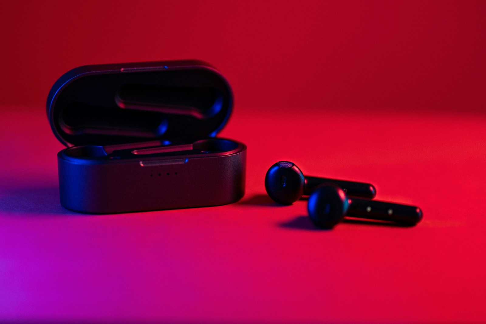 Black wireless earbuds and open charging case under red studio lighting