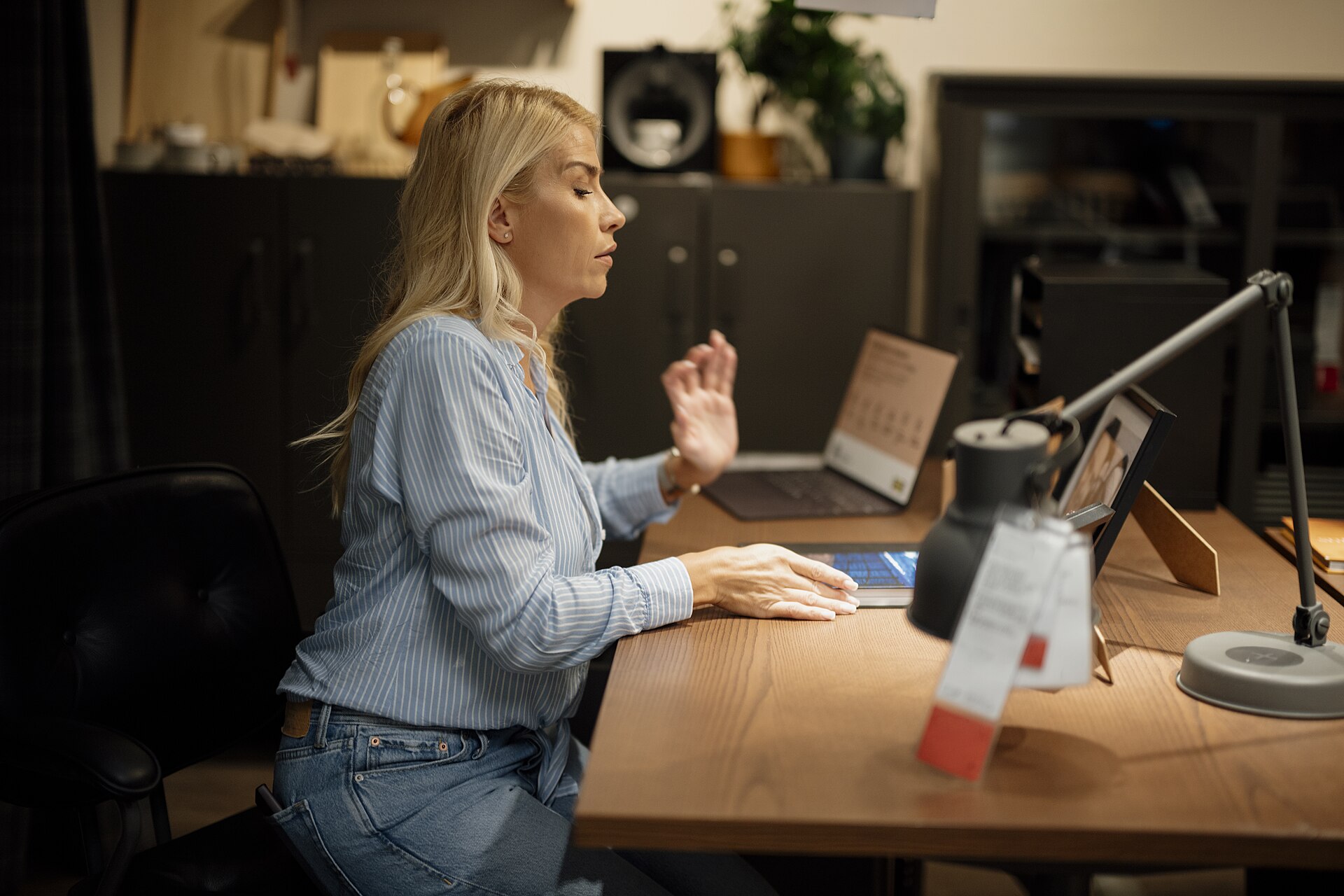 Woman working at a laptop on a wooden desk in a dimly lit home office