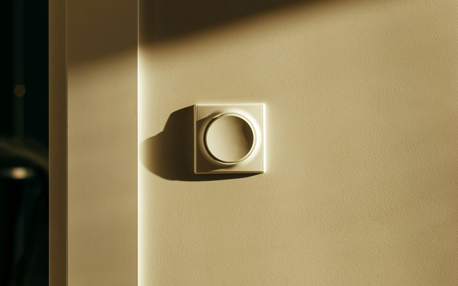 Round white light switch on a sunlit wall with a long shadow beside a doorway