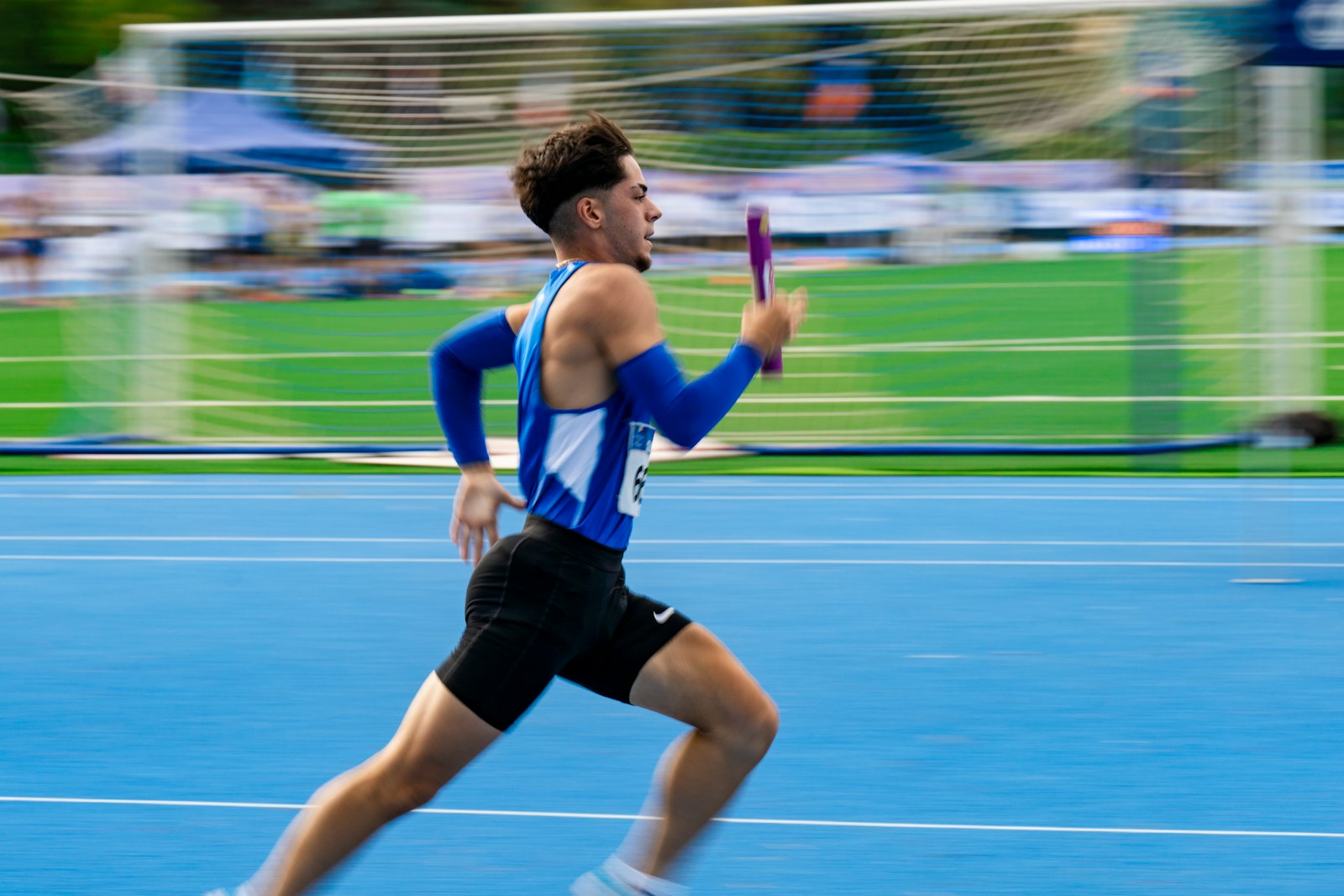 Sprinter in a blue singlet running on a blue track while holding a purple relay baton