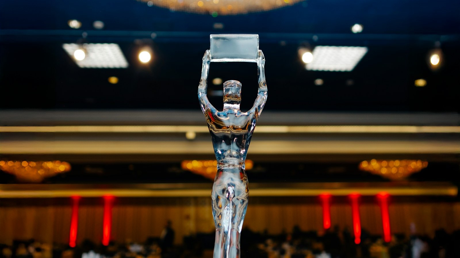 Glass award trophy on a stand in a ballroom with chandeliers and red stage lights