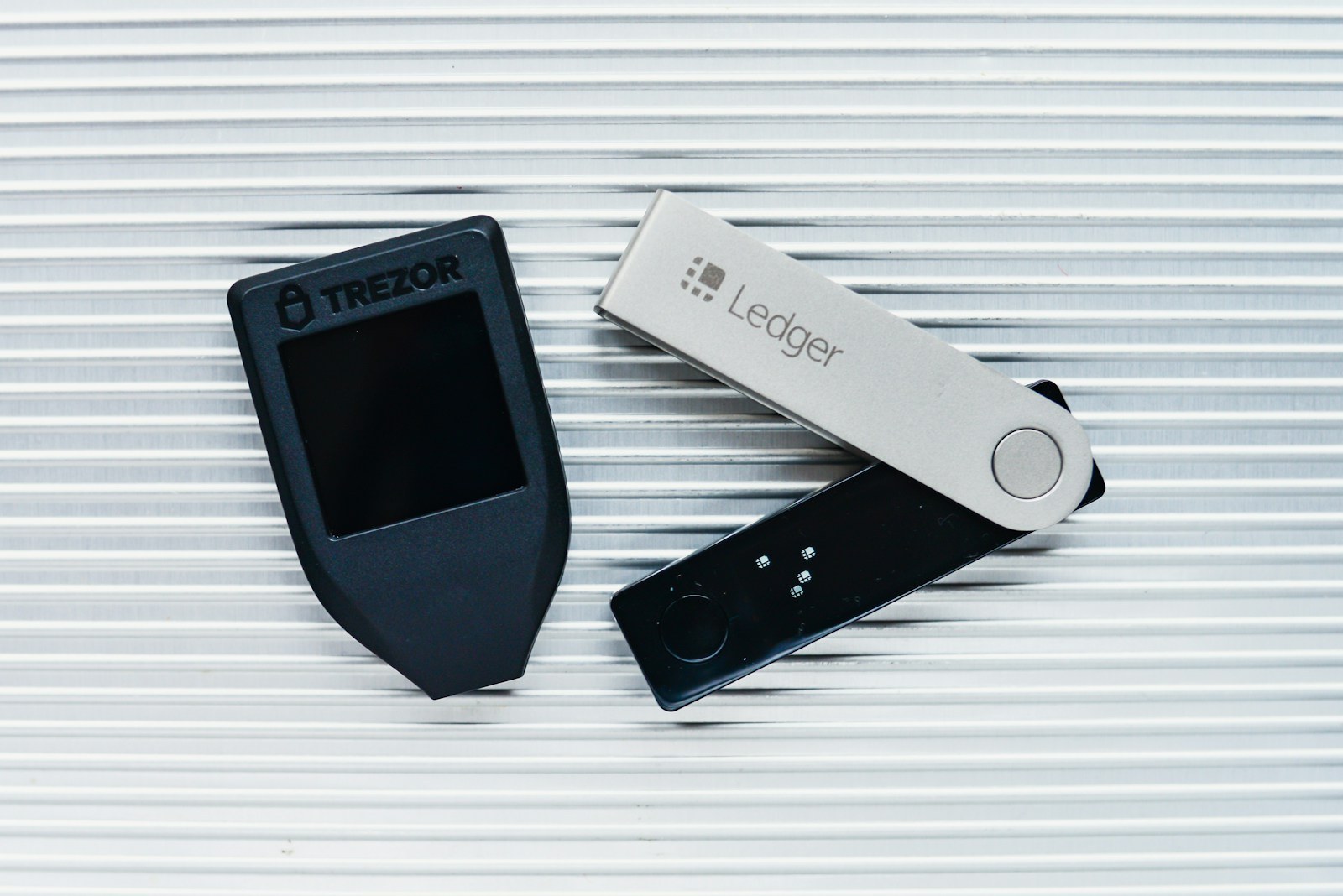 Trezor and Ledger hardware crypto wallets lying on a ridged metal surface
