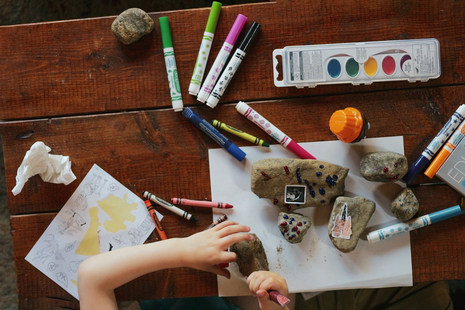 Child decorating rocks with markers and craft supplies on a wooden table
