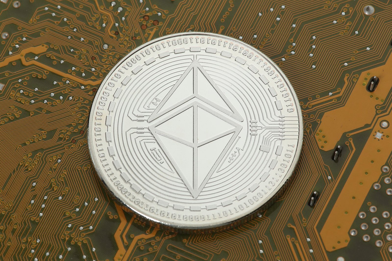 A silver Ethereum coin resting on a green and gold circuit board