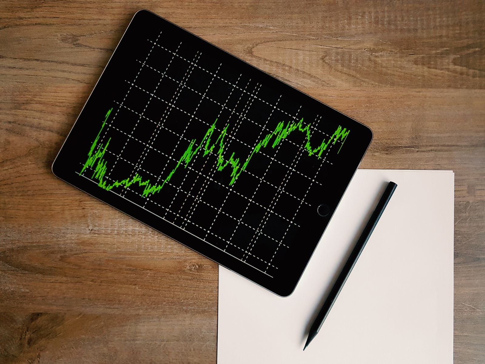 Tablet showing a green market line chart next to a pencil