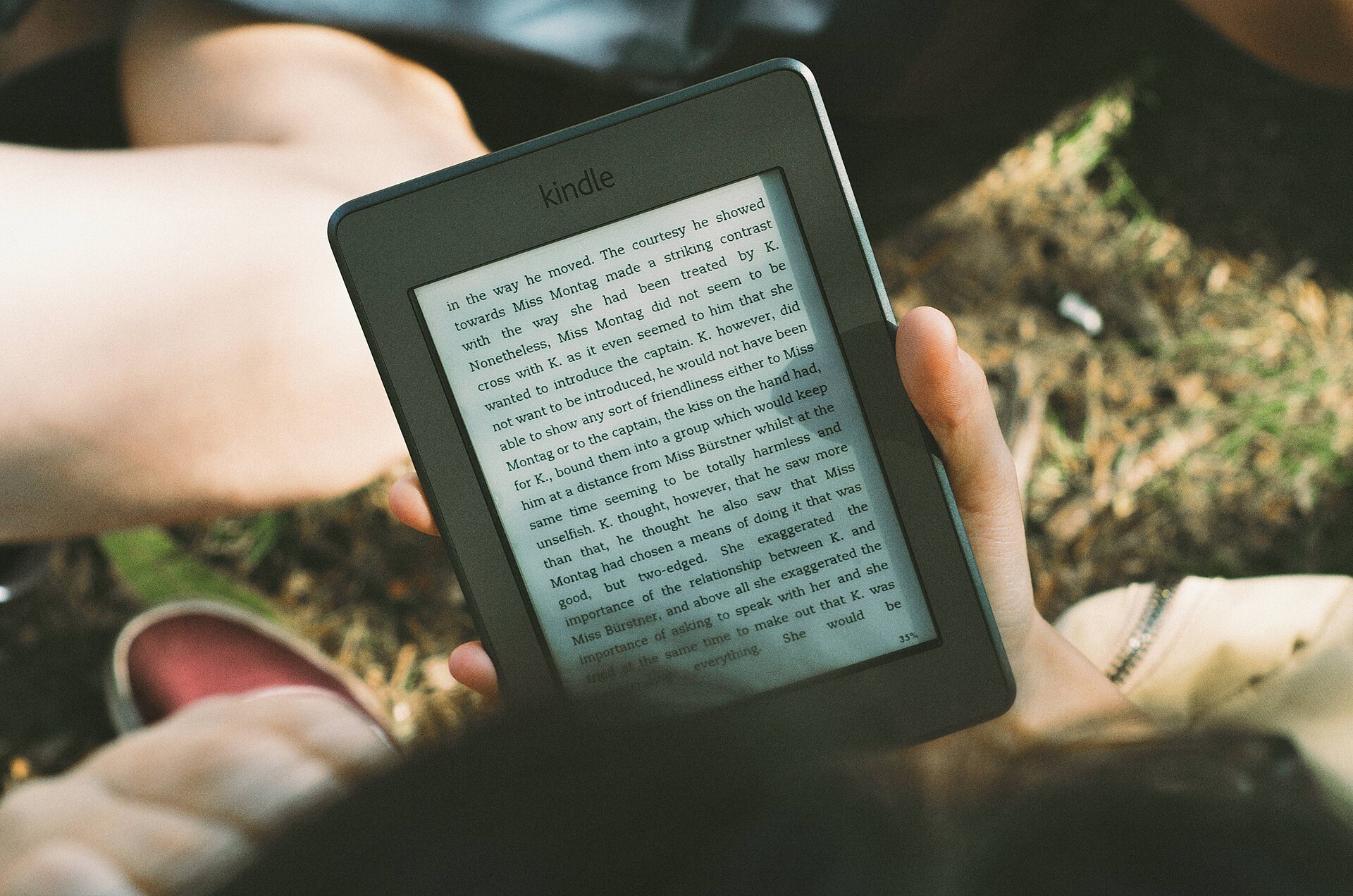 A person reading on a Kindle e-reader outdoors