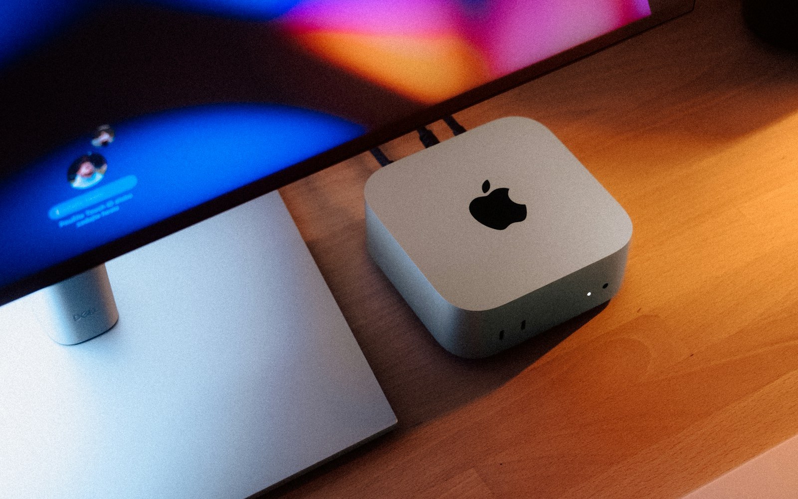 Silver Apple Mac mini on a wooden desk beside a monitor stand