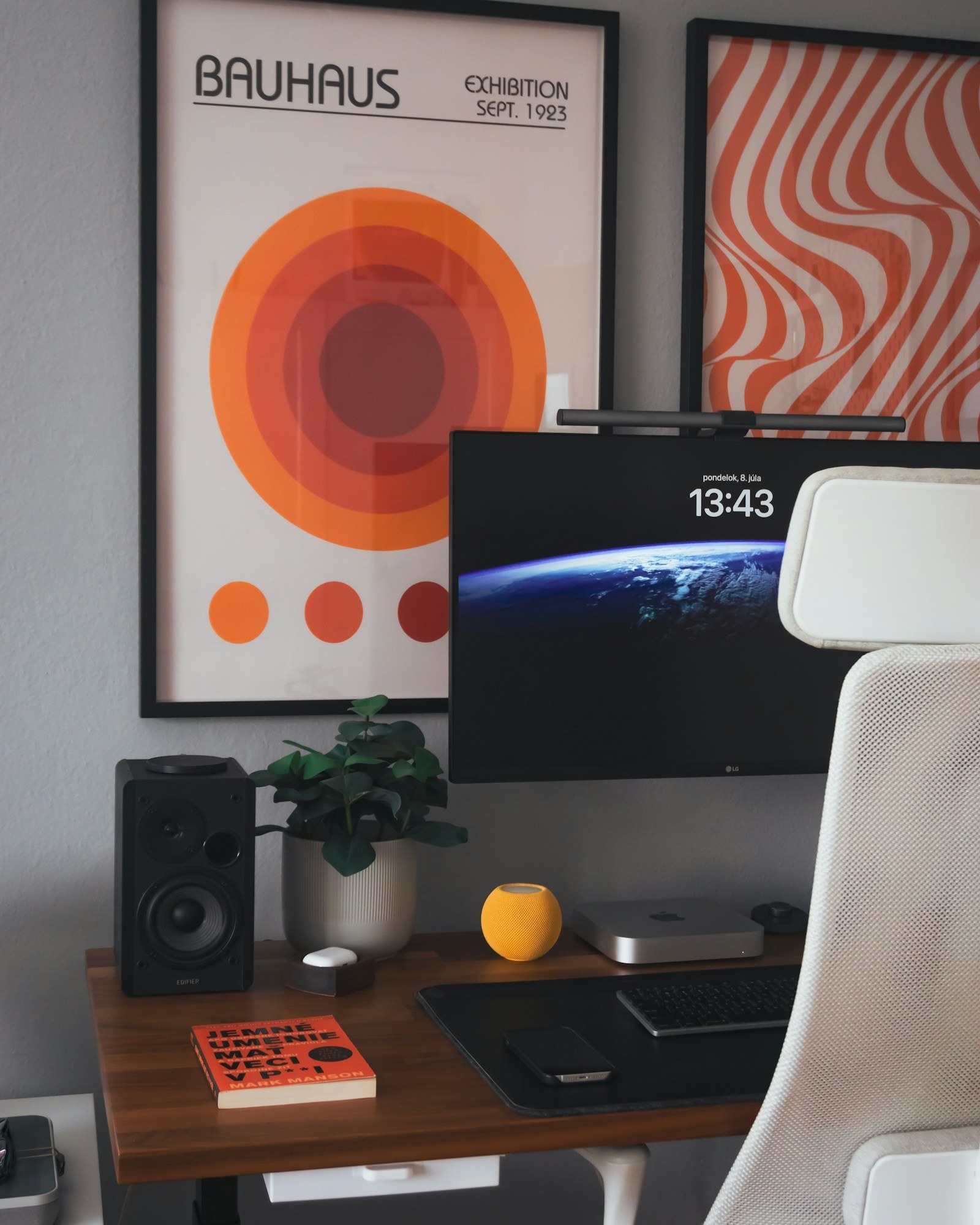 Home office desk with a Mac mini under a monitor, a speaker, a plant and framed Bauhaus posters