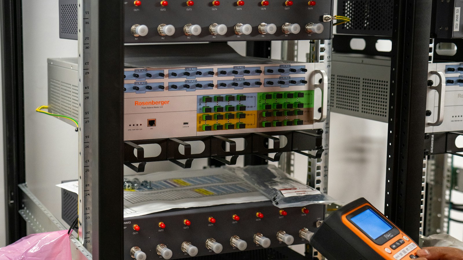 A technician points a handheld tester at networking equipment mounted in a server rack