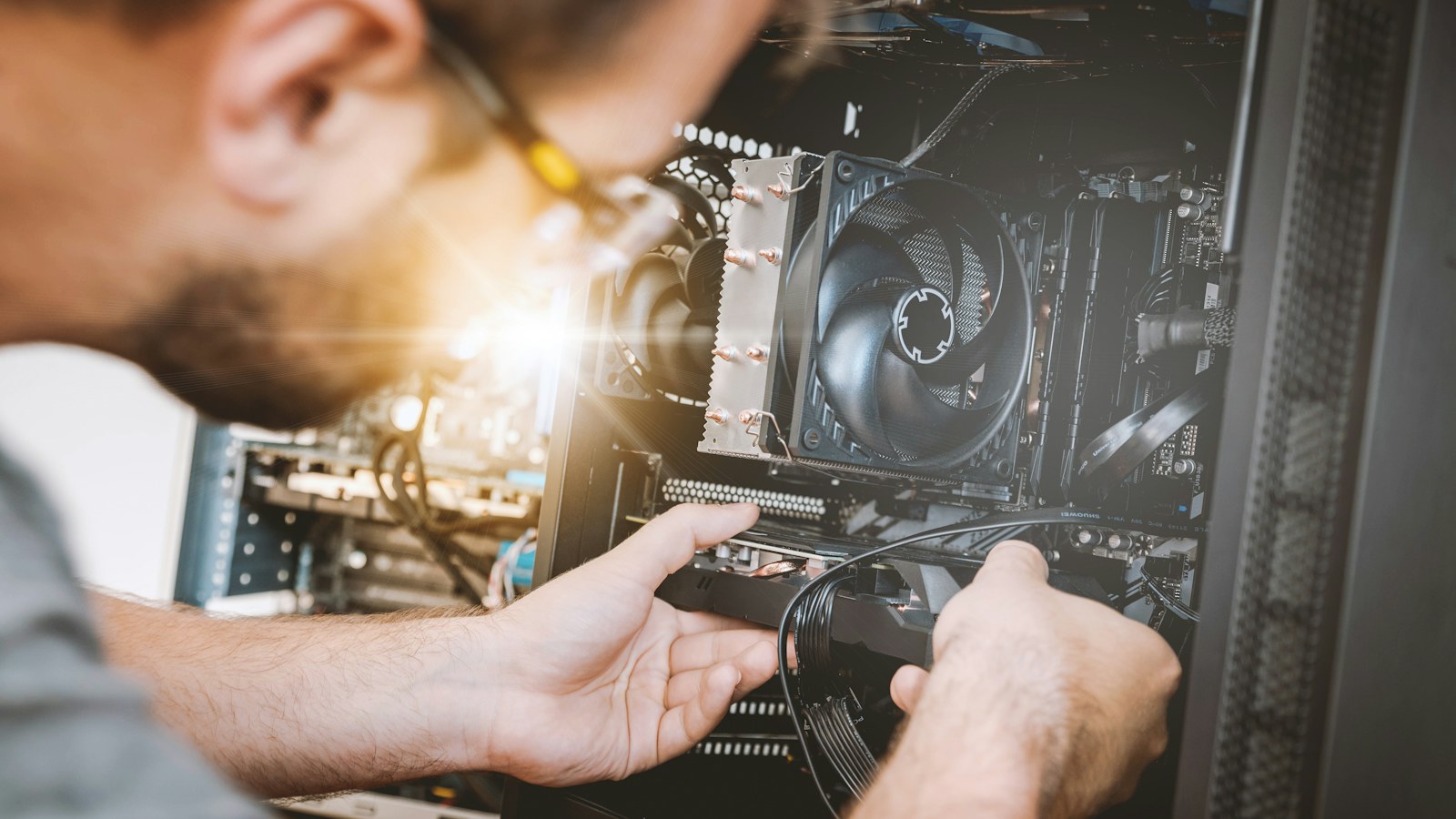 A person installs a graphics card into a desktop computer case next to a CPU cooler