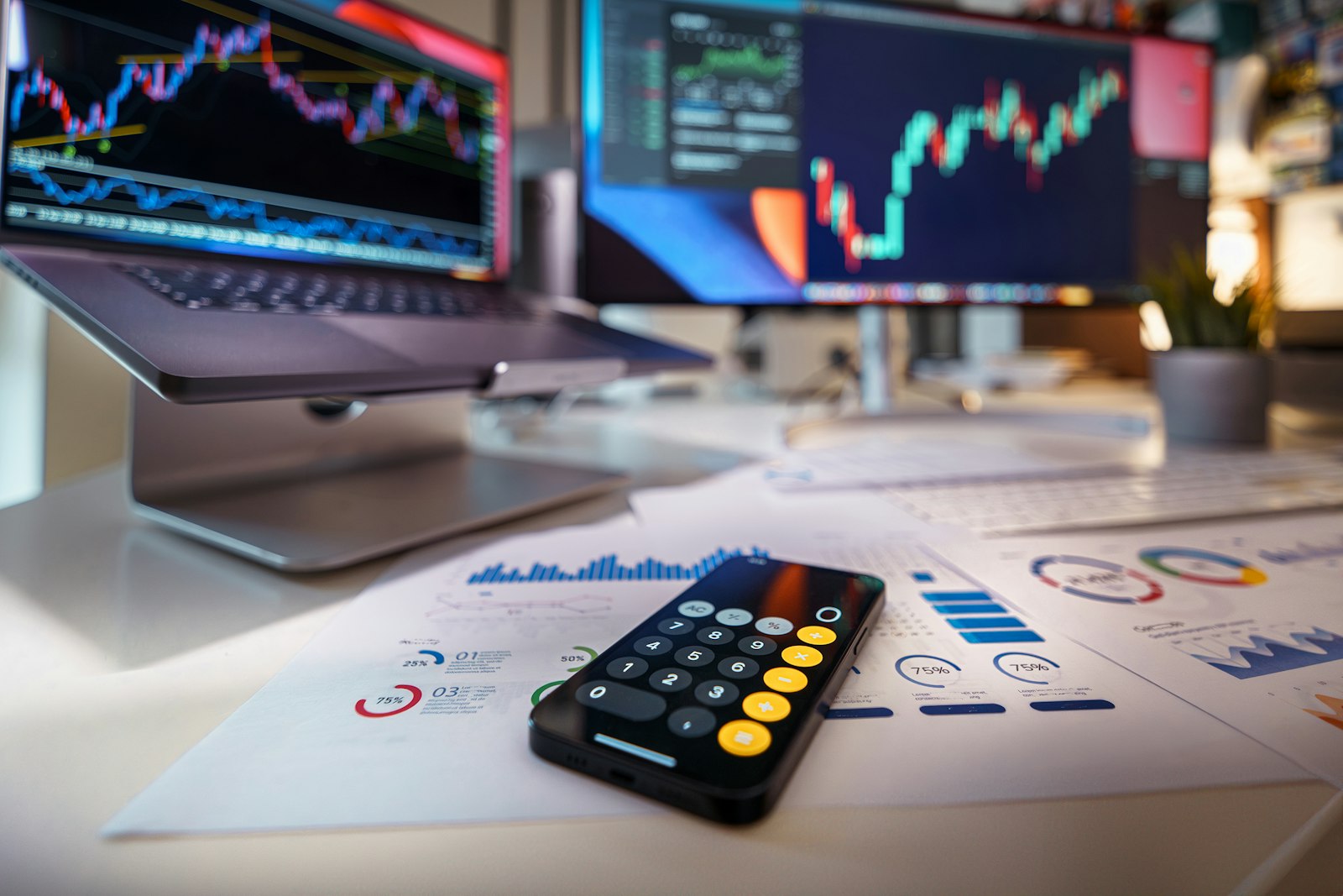 Smartphone calculator on printed charts with trading screens in the background