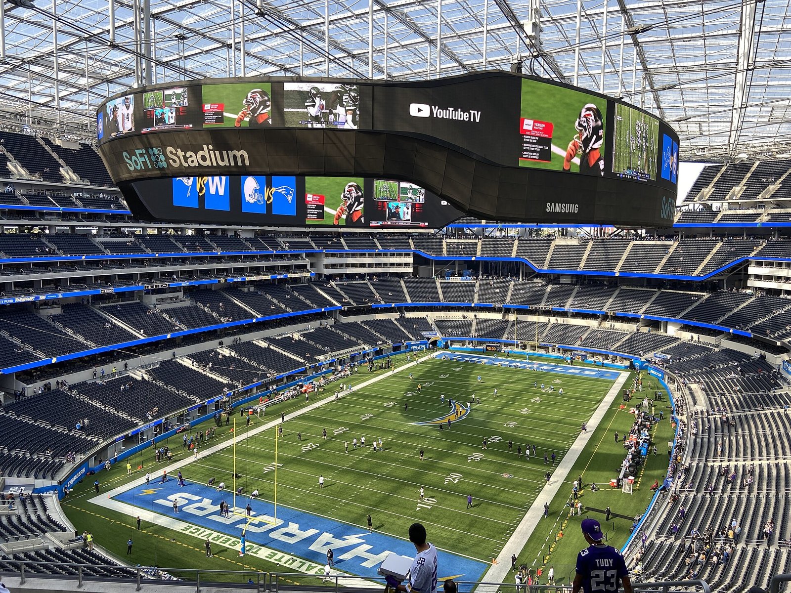 Inside SoFi Stadium during an NFL game, with the field below and the huge ring-shaped video board hanging under the roof