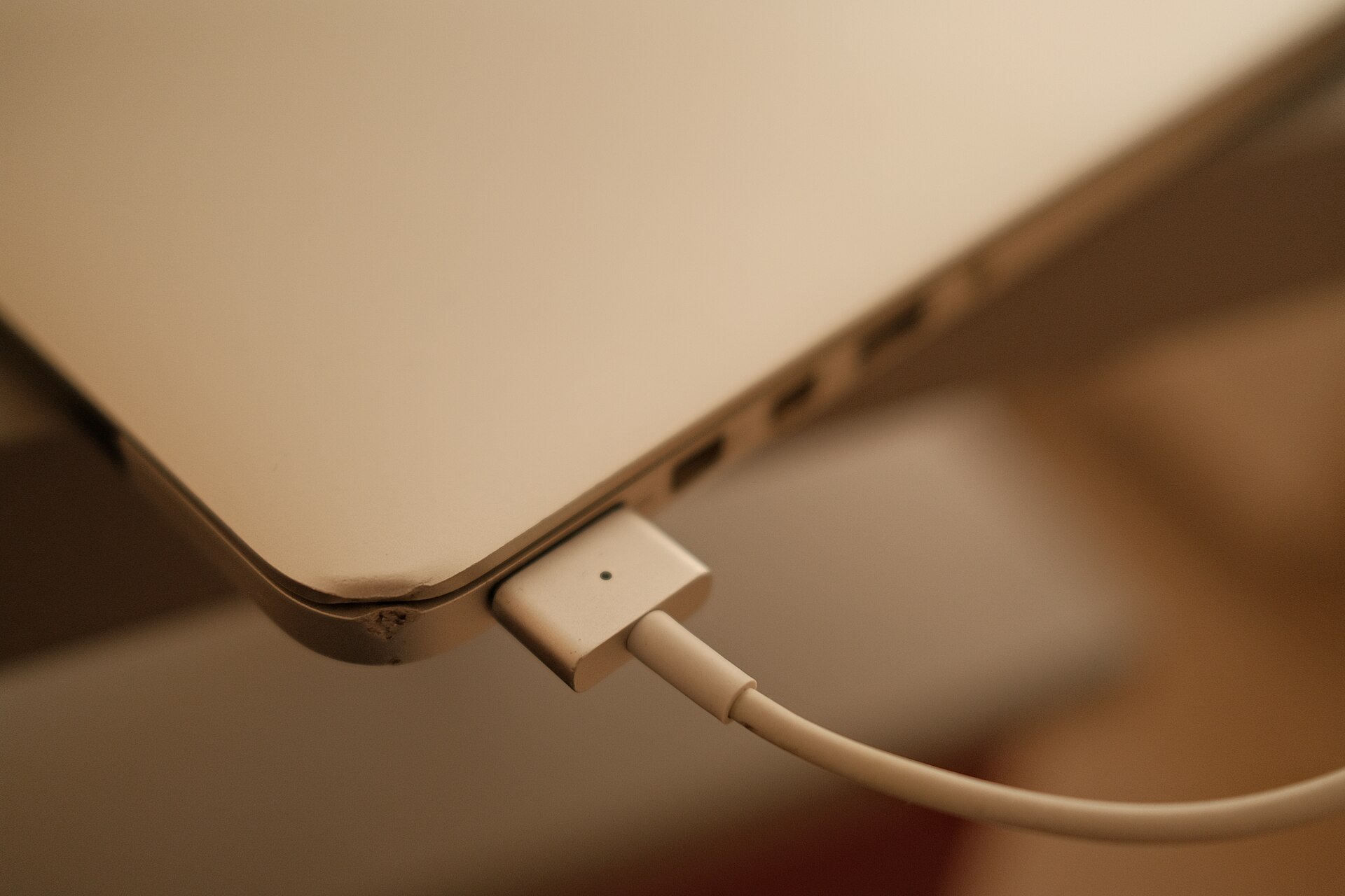 A white magnetic charging cable attached to the side port of a silver laptop