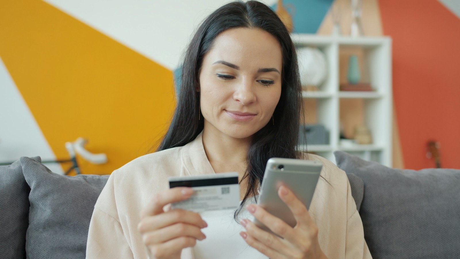 Woman on a sofa holding a credit card while shopping on her smartphone
