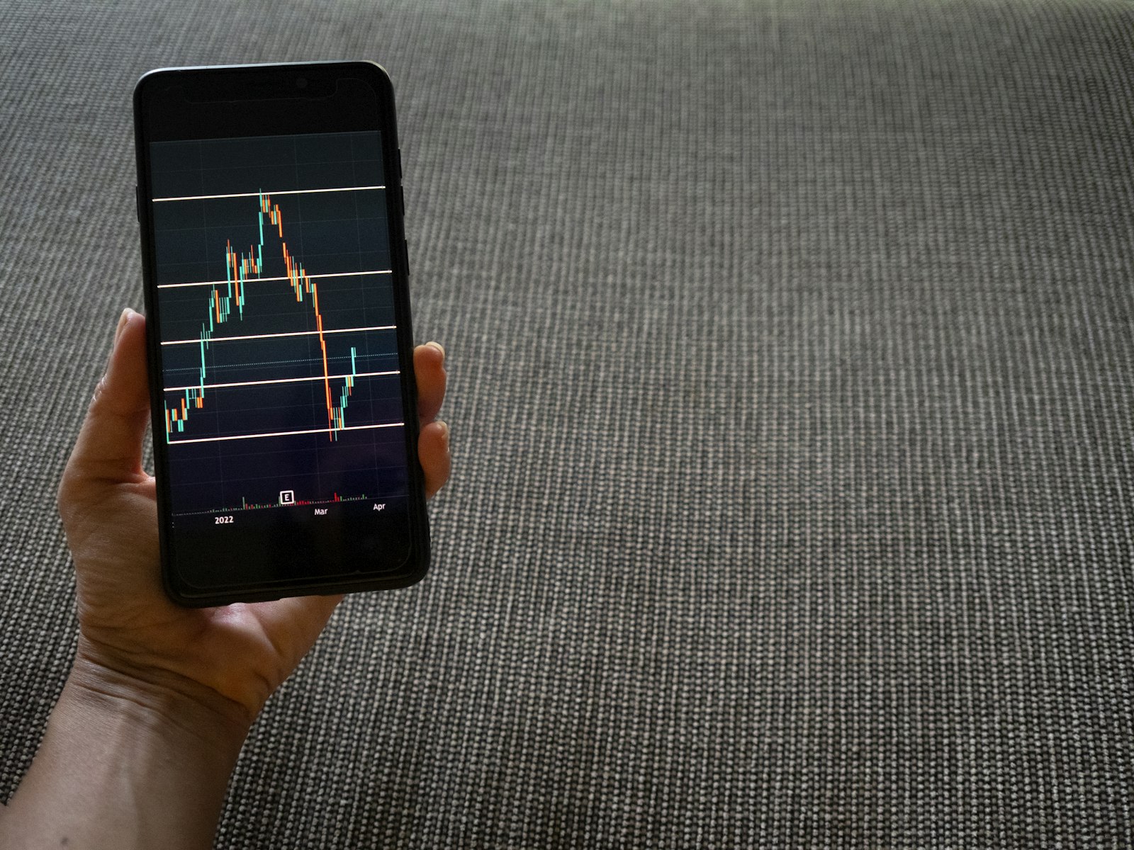 Hand holding a smartphone showing a stock trading chart